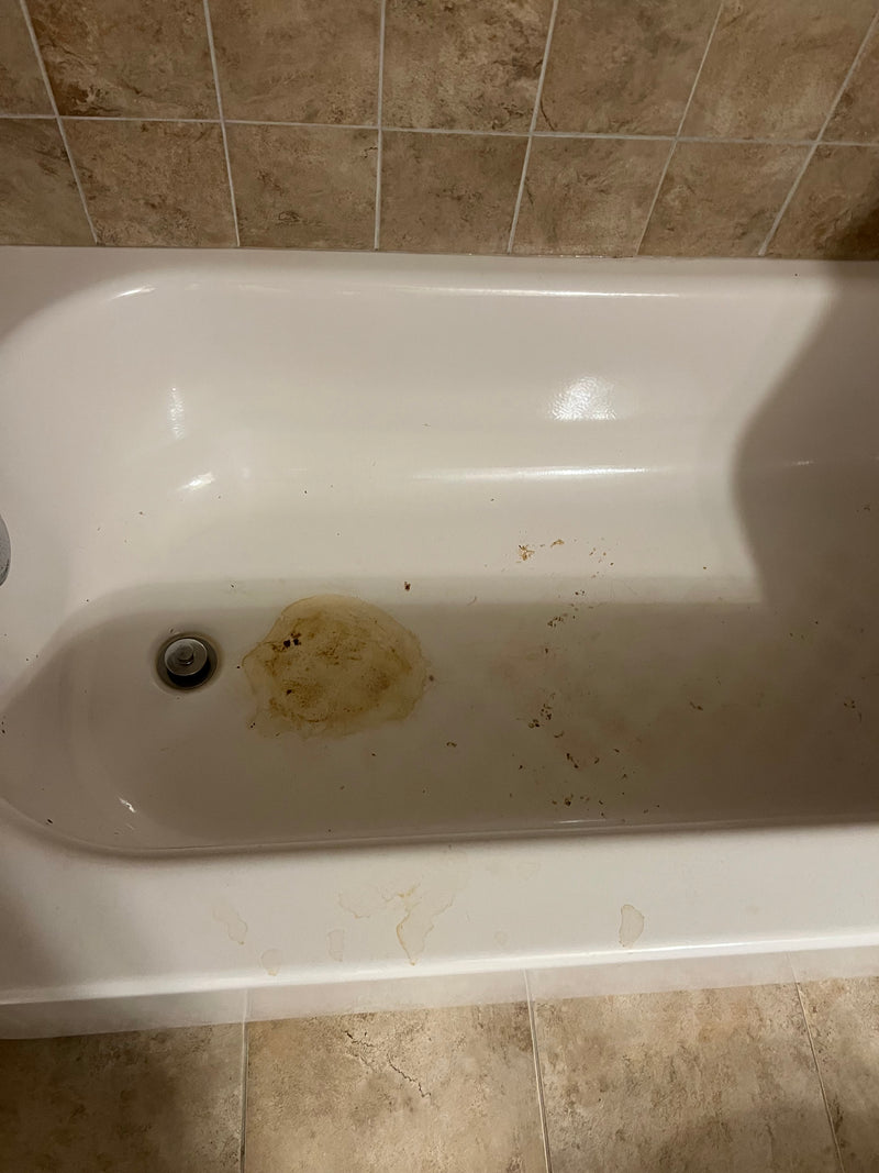 Dirty white bathtub against a tiled bathroom wall